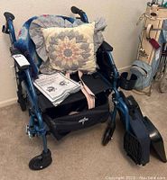 Blue Medline walker wheelchair with black seat, blue metal frame, wheels, hand brakes, storage pouch, footrest, and two cushions (one quilted and one crocheted)