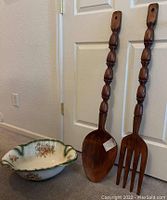 Shows the entire set at the base of a door, with the wooden fork and spoon standing vertically behind the porcelain basin, highlighting size and condition.