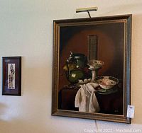 Both framed art pieces hanging on wall: a large still life oil painting and a smaller wood fiber slice art