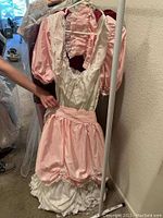 Pink and white vintage women's costume dress with puff sleeves, lace trim, and ruffled skirt on hanger.