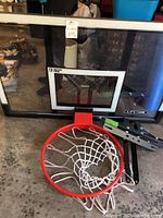 Front view of Lifetime branded clear basketball backboard with red rim and white net on concrete floor.