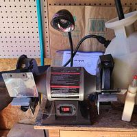 Photo of Task Force 6-inch bench grinder showing both grinding wheels, safety guards, on/off switch, and flexible lamp.