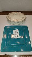 Photo of a cream-colored ceramic casserole dish with a lid featuring floral pattern, alongside an 11-inch square vibrant blue platter.