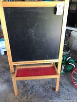 Full view of the Childress chalkboard with wooden frame standing upright on four legs, black chalk surface and red tray below.