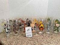 Front view showing 14 clear glasses with colorful Warner Brothers characters, arranged in a single row on granite surface