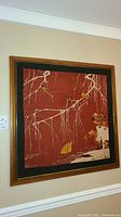 Framed decorative tapestry hanging on wall showing full piece with brown frame and black border.