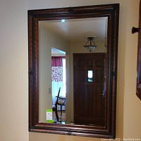 Frontal view of the large rectangular mirror with dark wood frame and reflective glass surface, showing part of the room reflected.