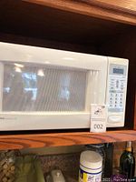 White Emerson microwave oven on wooden shelf showing front with digital control panel and window door