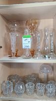 Display of various glass pieces including candlesticks, vases and votives on shelf