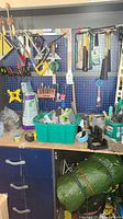 Workbench area with pegboard holding tools including hammers, screwdrivers, clamps, measuring tapes, and containers with small items.