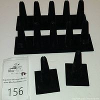 Two black velvet multi-ring display stands with five vertical holders each, and two black velvet single-ring stands with square bases on a light surface.