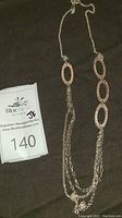 Full view of the necklace showing three large textured oval links connected by delicate silver chains, displayed on a dark fabric background with auction tag.