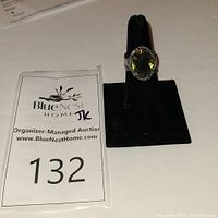 Front view of Silpada ring with green olivine on a black display stand alongside auction card.