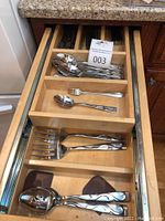 Top view of wooden kitchen drawer with organized sections containing multiple spoons and forks with wave patterned stainless steel handles.