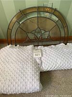 Photo showing stained glass arch window with chain for hanging behind folded white popcorn fabric pieces on carpet.