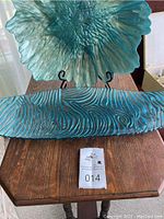 Top view of wooden table showing surface texture and two blue glass decorative pieces: a large ruffled bowl/plate and an elongated rectangular plate with swirling pattern.