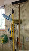 Wide view of cleaning tools including push broom, mop, and brushes mounted on pegboard by window