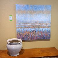 Photo showing abstract wall art and ceramic pot on a wood surface against a beige wall.