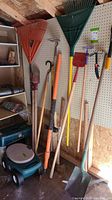 Wall with various garden tools including rakes, shovels, hoes, a machete, and a garden scooter.