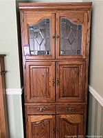 Full view of tall wooden display cabinet with four doors and two drawers, featuring stained glass on top doors and wooden panels on lower doors.