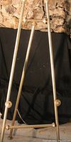 Metal adjustable easel standing upright, tripod structure with chain support and knob adjustment.