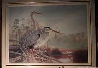 Photo of framed wildlife art print showing two herons near a water body in a natural setting with muted earth tone colors and custom matting.