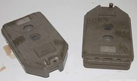 Two camouflage colored motion activated trail cameras side by side on white background, showing front sensors and lenses.