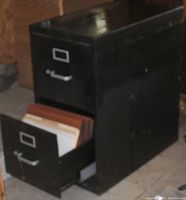 Photo of a black metal two drawer file cabinet with one drawer partially opened showing hanging file folders inside.