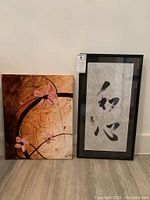 Photo showing mixed media canvas with pink blossoms and framed calligraphy art side by side.