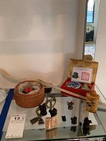 Wide view of Asian collectibles including Buddha necklace, metal figurines, riding crop, boxed John name stamp, and etched jar on glass table.