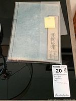 Photo of antique Japanese book covered in translucent sheet, showing handwritten calligraphy and label with date '1780' handwritten on sticky note.