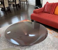 Overall view of round cocktail table with tinted glass top and metal pedestal base in front of sofa