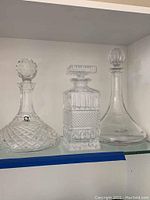 Three lead crystal decanters displayed side by side on a shelf