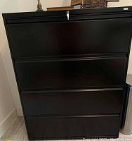 Front view of black metal file cabinet showing four drawers and lock at the top with keys inserted.