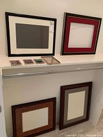 Black and red matted picture frames on a white shelf along with smaller frames and samples below