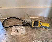 Yellow VistaQuest DVR-2A optical probe scope device with flexible black cable and camera probe at the end, displayed alongside user manual on a hard surface.