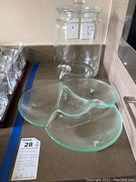Glass beverage server with metal spigot and divided glass condiment server with metal feet next to it on countertop.