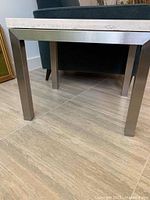 Side view showing the metal base of the side table with squared metal legs and dark finish.