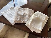 Three folded tablecloths and napkins arranged on table, showing different fabric textures including damask and plain weave.