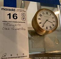Front view of brass-tone metal trinket box lid with Tiffany & Co. clock face design and numerals