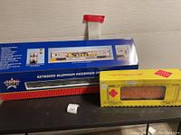 Boxed USA Trains extruded aluminum passenger car in blue/red packaging alongside yellow Aristo-Craft box car packaging.