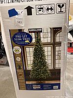 Box showing image and details of 9 ft Kirkland Signature pre-lit slim Christmas tree with 1250 constant on GE bulbs.