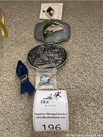 Photo showing Alaska-themed belt buckles, pins, and a blue fabric accessory arranged on carpet.
