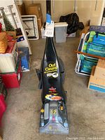 Front view of black Bissell ProHeat carpet shampooer upright on garage floor showing brand labels and specifications.