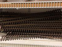 Various curved and straight G6 scale model railroad tracks stacked on shelf with wooden ties and metal rails.