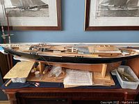 Side view photo of the homemade scale model sailboat on a wooden stand with parts and plans nearby.