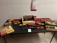 Photo showing multiple HO scale Lionel and various other scale train cars along with boxed accessories on a table.
