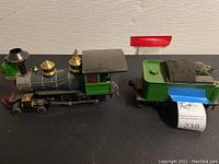 Side view of green HLW train engine and coal car on black surface with some wear and dust