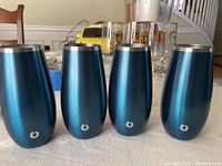 Four blue Snowfox stainless steel cups lined up on a table showing the front with logo.