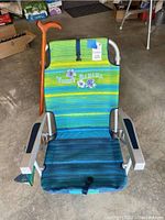 Front view of the Tommy Bahama beach chair showing colorful striped fabric and attached cane leaning beside it.